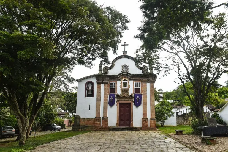 Igreja de Nossa Senhora do Rosário, em Tiradentes, entre árvores e com calçamento de pedra