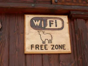 Placa de madeira entalhada com a palavra Wi-Fi e o desenho de uma ovelha, presa a uma parede de tábuas