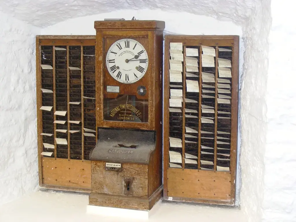 Relógio de ponto antigo entre dois porta-cartões de madeira, exposto em museu