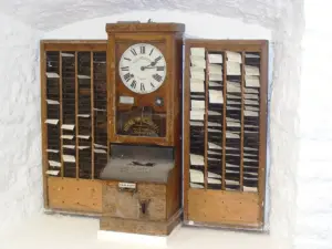 Relógio de ponto antigo entre dois porta-cartões de madeira, exposto em museu