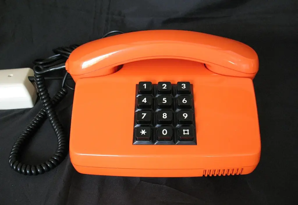 Telefone fixo laranja de teclas, com o fone no gancho, sobre fundo preto