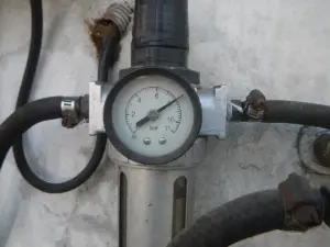 Manômetro de um compressor de ar de posto, preso à parede e ligado às mangueiras