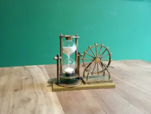 Ampulheta decorativa ao lado de uma pequena roda de metal sobre uma mesa de madeira