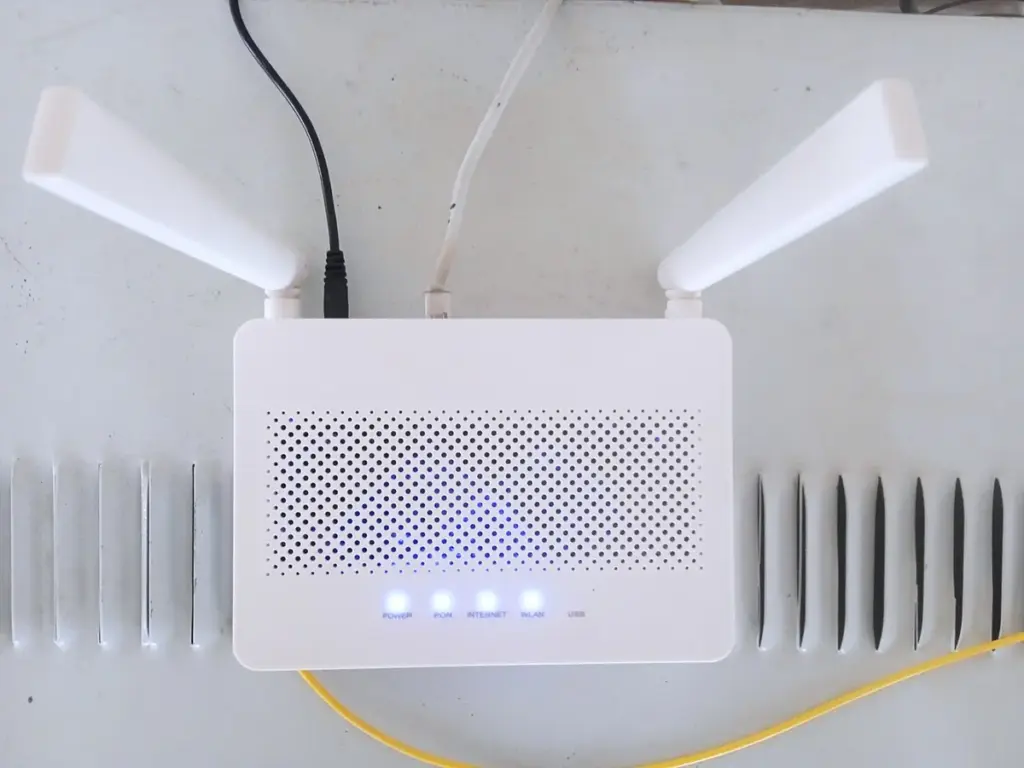 Roteador de Wi-Fi branco com duas antenas e luzes azuis acesas, com os cabos ligados