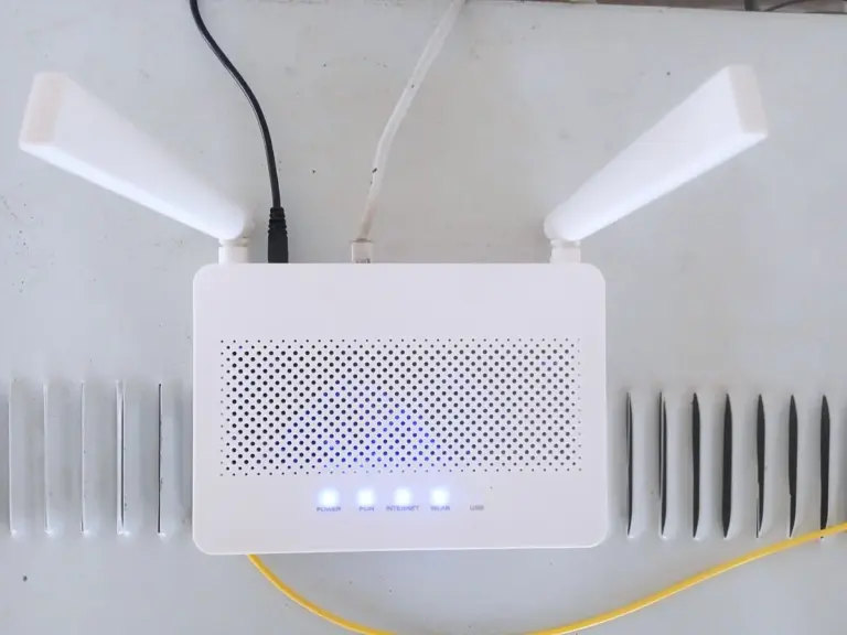 Roteador de Wi-Fi branco com duas antenas e luzes azuis acesas, com os cabos ligados