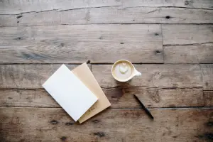 Cadernos, caneta e xícara de café sobre uma mesa de madeira, vistos de cima