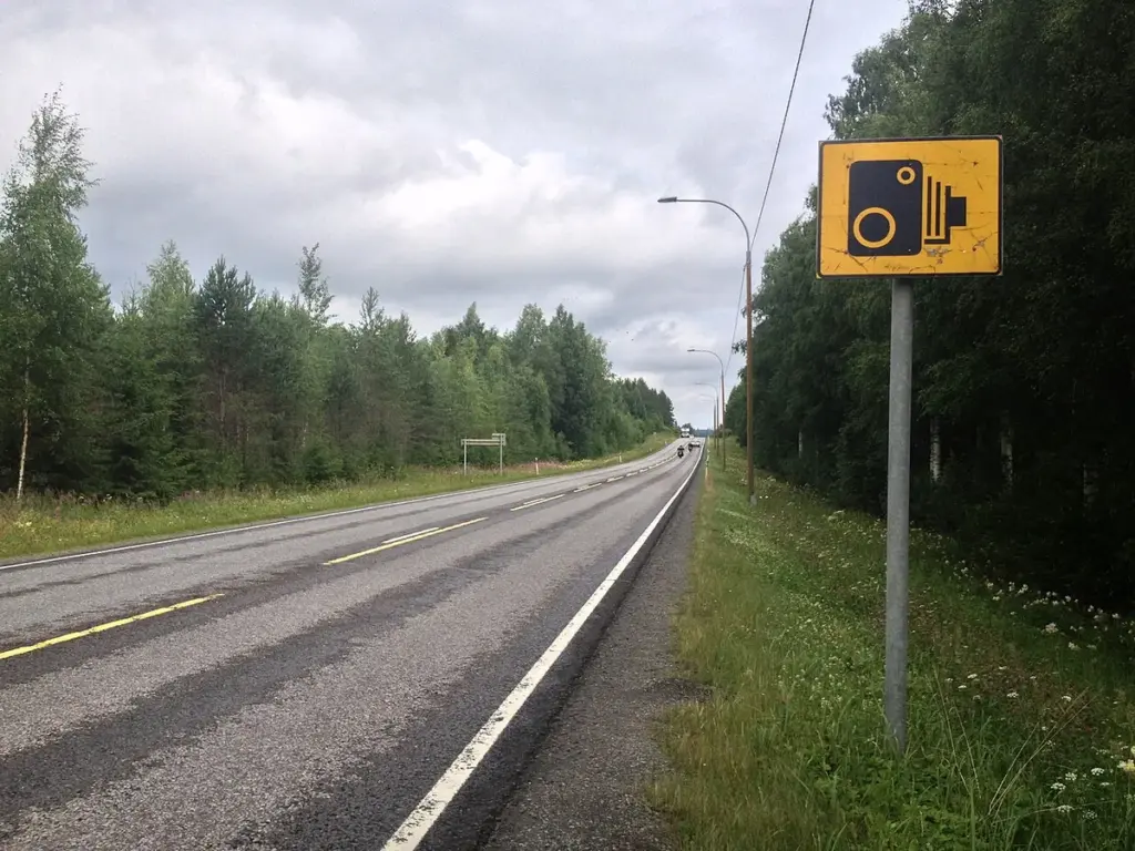 Placa de aviso de radar à beira de uma rodovia de pista simples cercada de mata