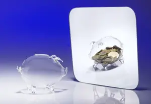 Dois cofrinhos de vidro em forma de porco, um com moedas e outro vazio, sobre fundo azul