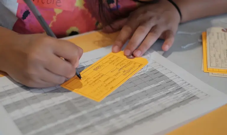 Mãos preenchem uma ficha de papel sobre uma mesa com formulários