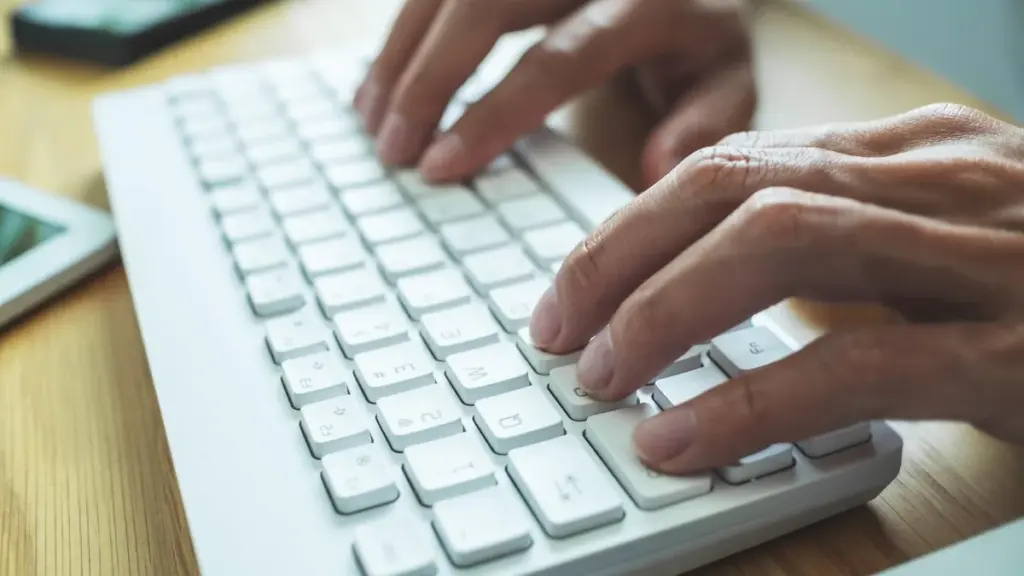 Mãos digitam em um teclado branco